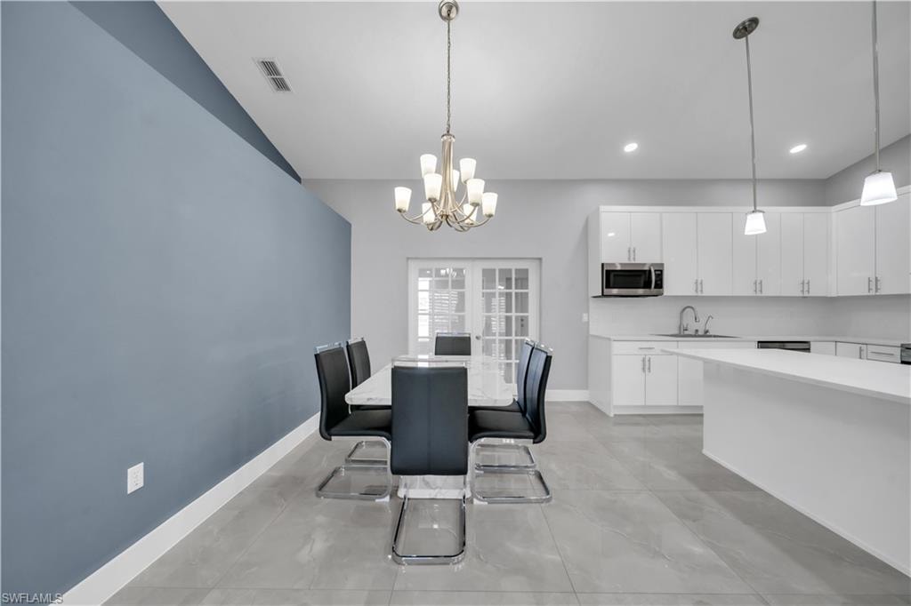 Open-concept living space with light gray tile flooring, a white kitchen island, and white shaker-style cabinetry with stainless steel appliances