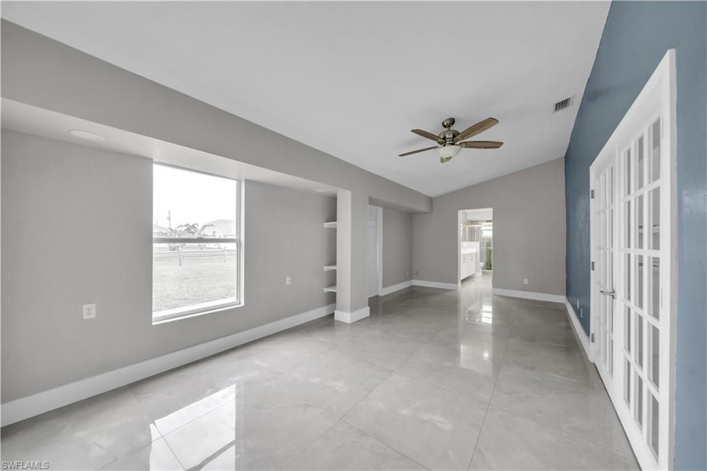 Vaulted ceiling with a ceiling fan, light gray wall paint, built-in shelving, French doors, and polished tile flooring