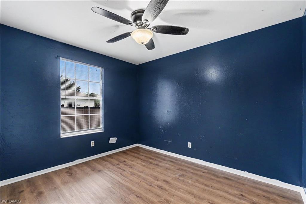 Room featuring wood-finish flooring, a ceiling fan with integrated lighting, and a large window with horizontal blinds