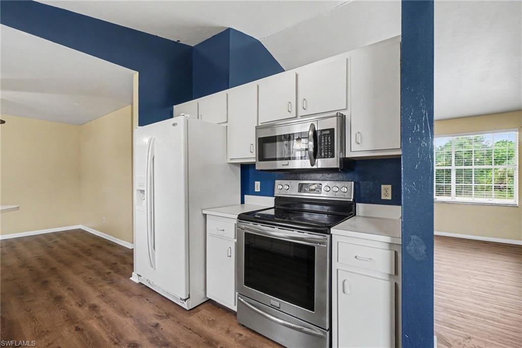 Kitchen featuring white cabinetry, stainless steel microwave, stainless steel electric range, white countertops, and wood-finish flooring