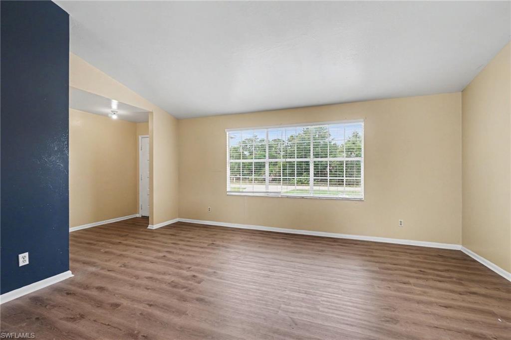 Interior featuring wood-finish flooring, vaulted ceilings, a large window with horizontal blinds, and a neutral color palette with an accent wall