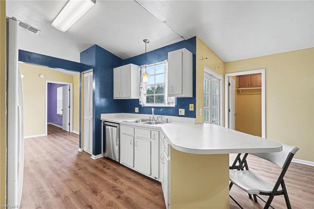 Kitchen featuring wood-finish flooring, white cabinetry, stainless steel dishwasher, a window over the sink, and a peninsula countertop