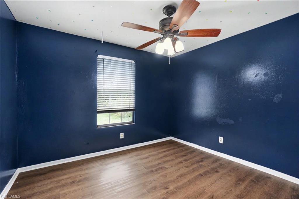 Interior room featuring dark blue walls, wood-finish flooring, a ceiling fan with light fixture, and a window with horizontal blinds