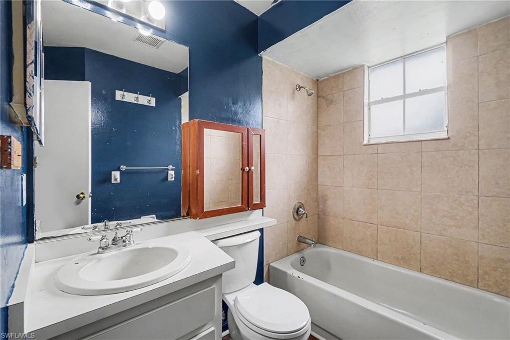 Bathroom featuring a white vanity with an integrated sink, a built-in medicine cabinet, a full-size bathtub, and tiled shower walls