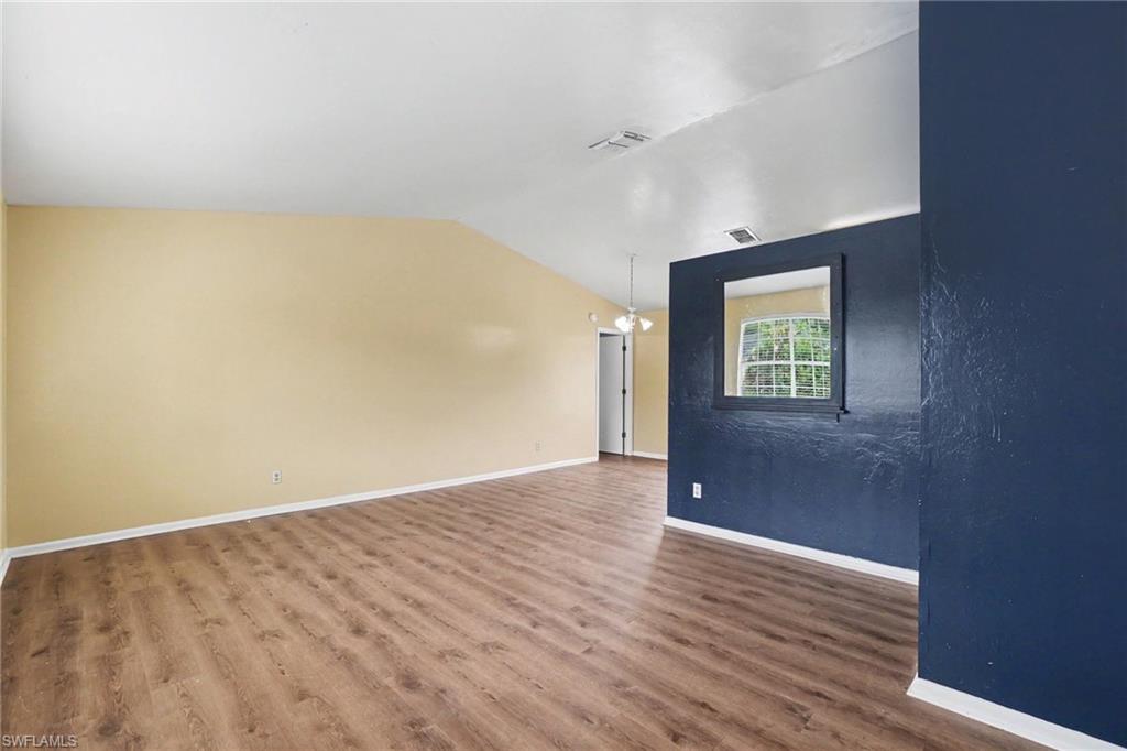 Spacious interior with wood-finish flooring, vaulted white ceilings, and a light-colored wall