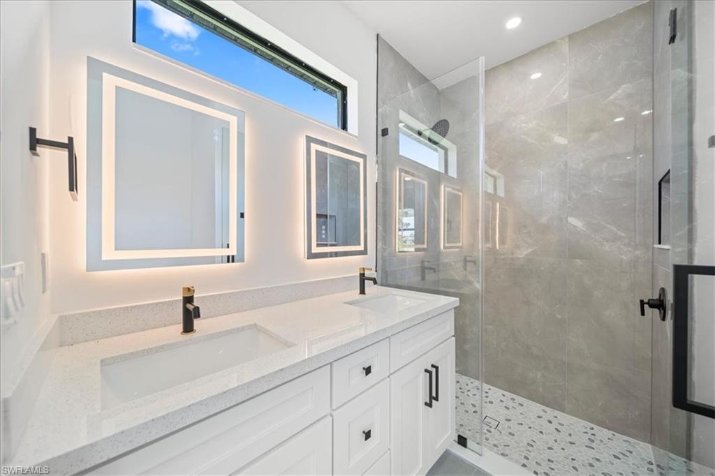 Spa-inspired bathroom featuring a dual-sink quartz vanity, illuminated designer mirrors