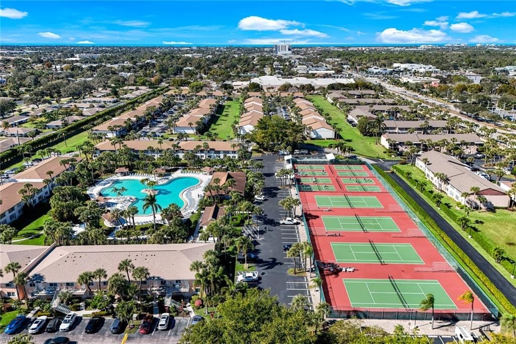 Aerial view of this resort-style community amenity area featuring multiple clay tennis courts with professional-grade surfacing, resort-style swimming pool with surrounding lounge deck, mature landscaping with palm trees throughout, and dedicated parking facilities