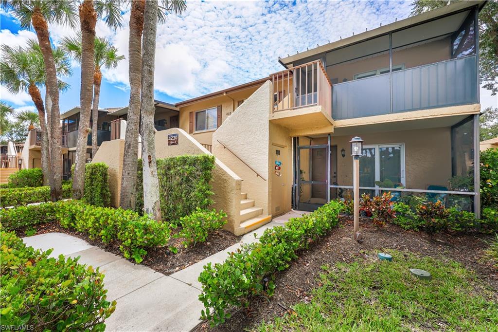 Contemporary condo featuring a manicured front landscape with mature palm trees, lush hedging, and defined concrete walkway