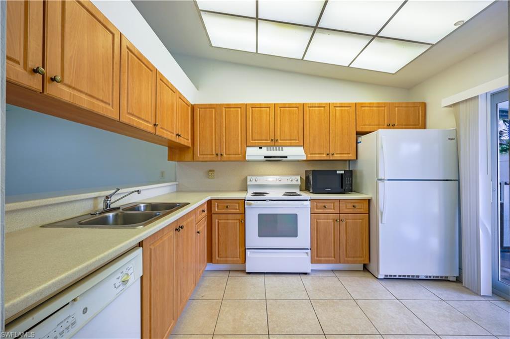 Spacious kitchen featuring warm wood-finish cabinetry, tile flooring, and stainless steel appliances including a white electric range and refrigerator