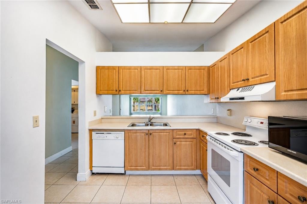 Kitchen featuring wood-finish cabinetry, tile flooring, and a comprehensive appliance suite including a dishwasher, range, and range hood