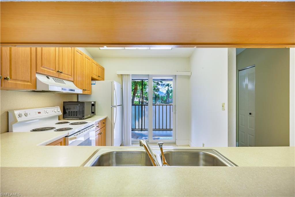 Kitchen featuring wood cabinetry, white appliances, a double basin stainless steel sink, and light-toned countertops
