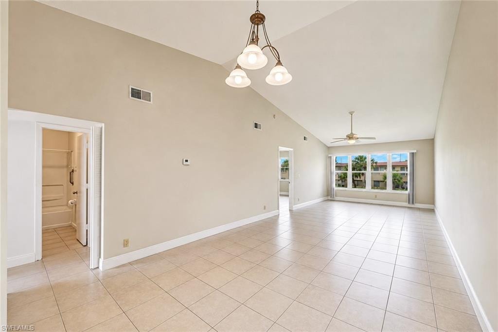 Spacious open-concept room featuring vaulted ceilings, tile flooring throughout, and abundant natural light from multi-pane windows