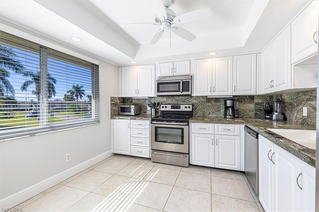 Kitchen featuring appliances with stainless steel finishes, white cabinets, a tray ceiling, light tile patterned floors, and ceiling fan