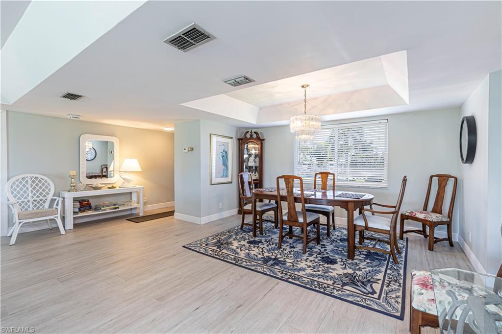 Dining area with a tray ceiling, a chandelier, and light wood-style flooring
