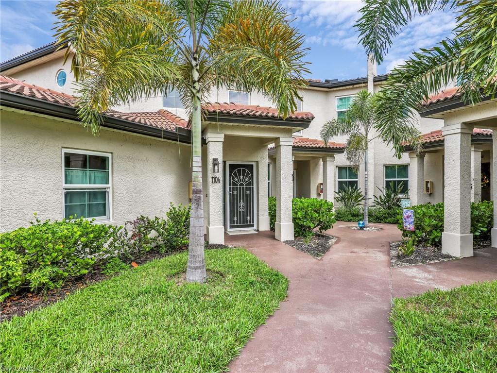 Stucco exterior with a tile roof, covered entryway, palm trees, and established landscaping