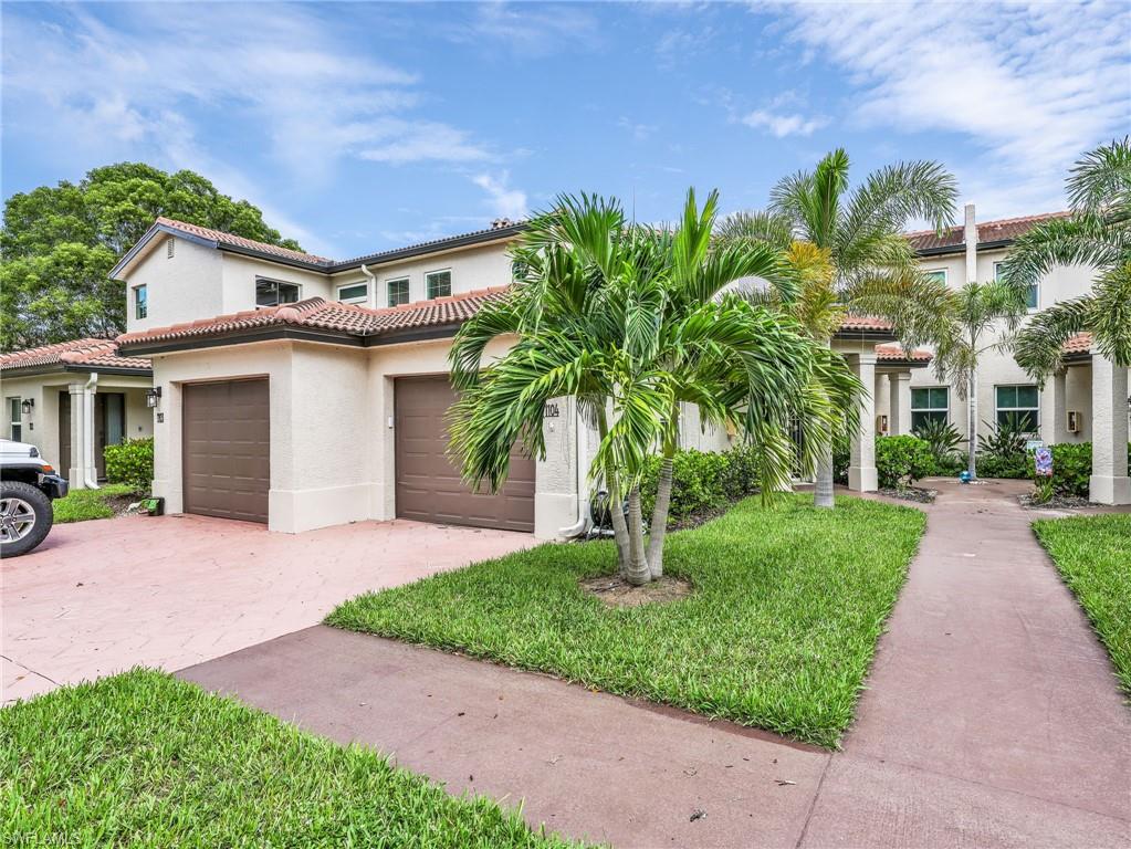 Mediterranean-inspired residence featuring a stucco exterior with clay tile roofing, dual two-car garage with dark panel doors, and lush tropical landscaping including mature palm trees and manicured lawn areas