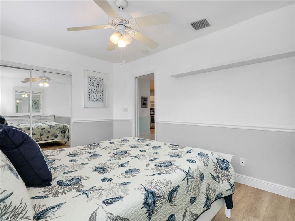 Wood-finish flooring, ceiling fan with integrated lighting, mirrored sliding closet doors, chair rail detailing, and a wall-mounted display shelf