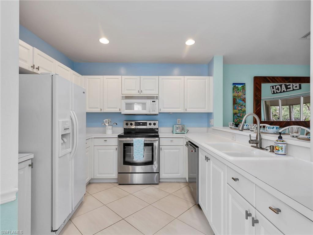 White cabinetry with brushed nickel hardware, stainless steel appliances, light-toned countertops, and recessed lighting