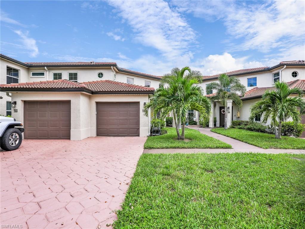 Impressive two-story residence showcasing a dual-garage driveway with herringbone paver detailing, lush manicured lawn, and mature palm landscaping
