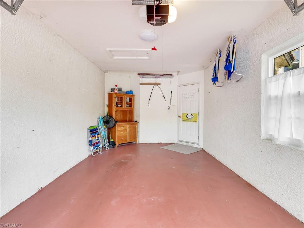 Attached single-car garage with a red-toned floor, a side-entry door, and a window with privacy curtains