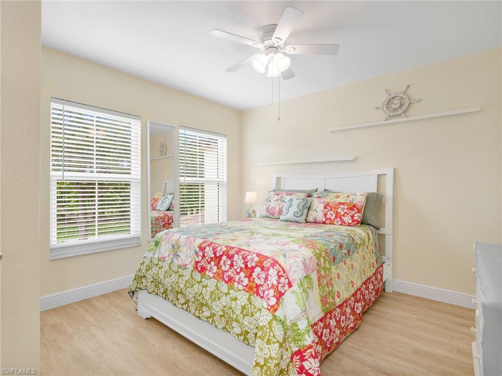 Recessed lighting, wood-finish flooring, white ceiling fan with integrated light, two windows with blinds, and a white headboard