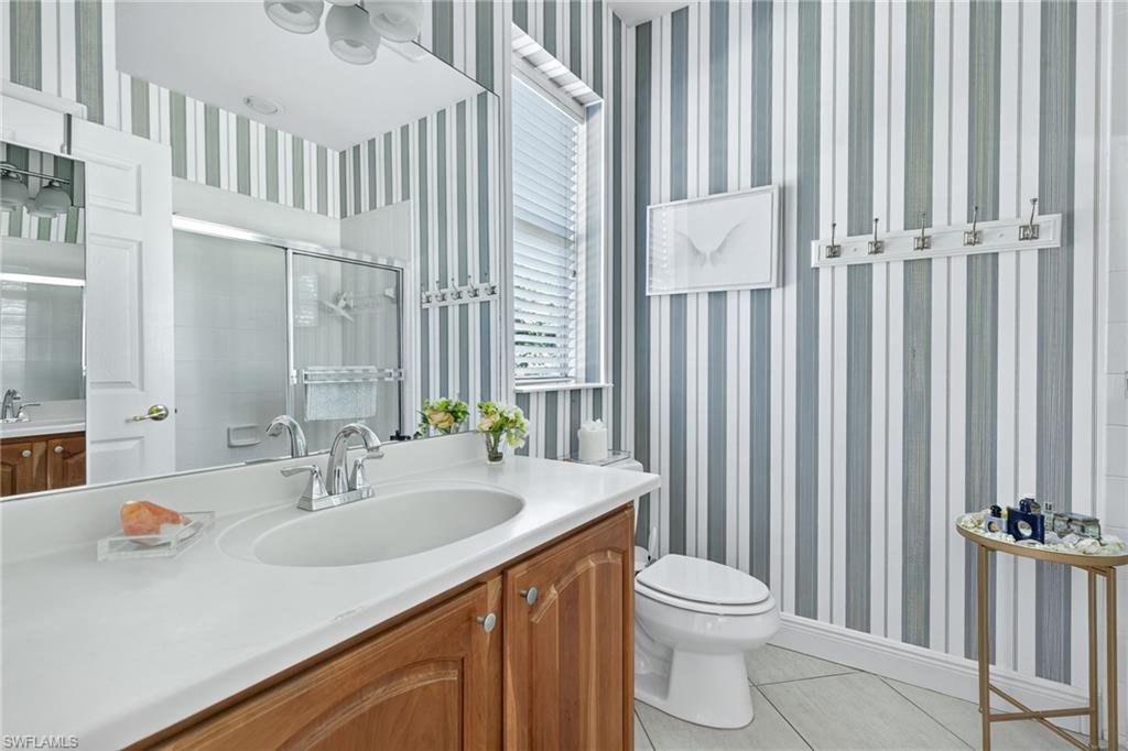 Full bathroom featuring wallpapered walls, light tile patterned floors, vanity, and a shower stall