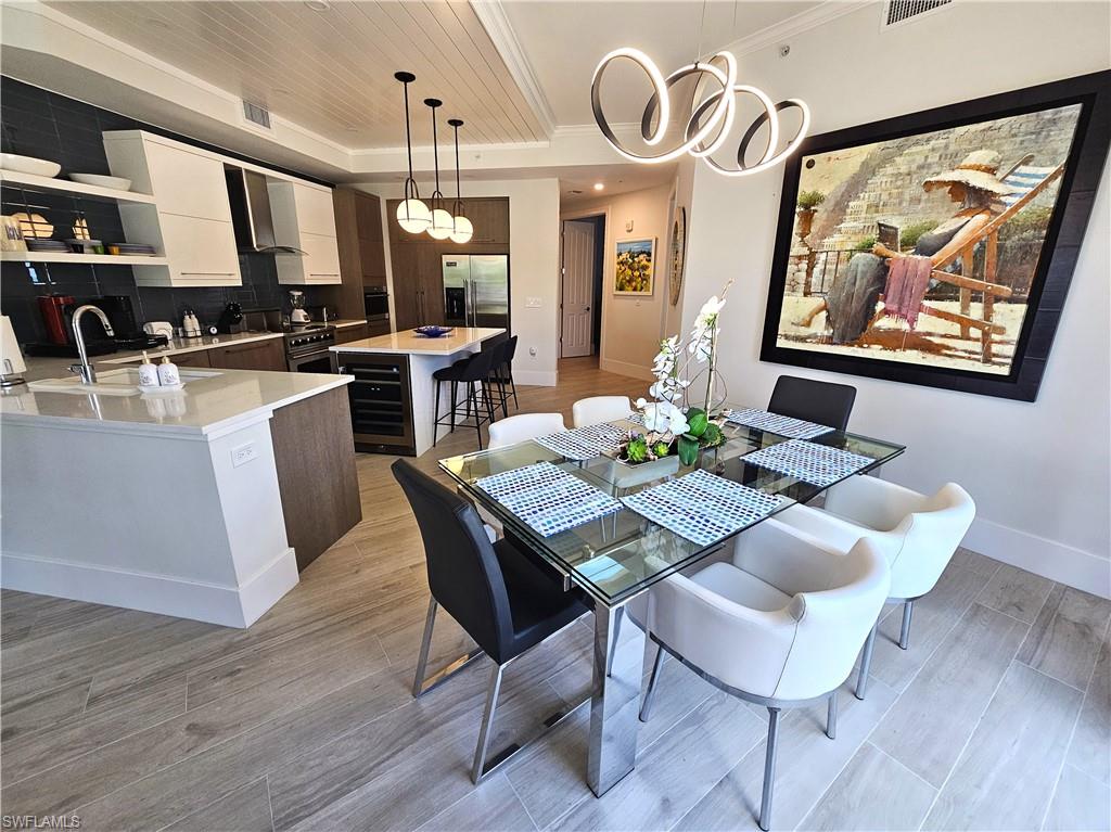 Dining room with light wood finished floors, beverage cooler, and ornamental molding