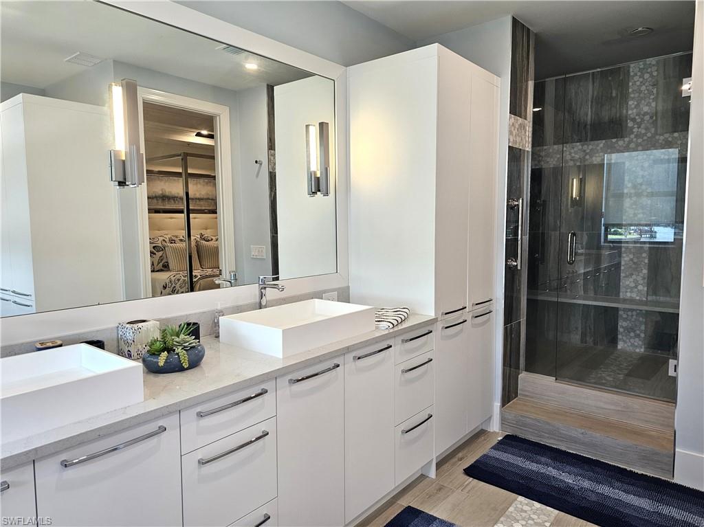 Ensuite bathroom with double vanity, a shower stall, and light wood-style flooring