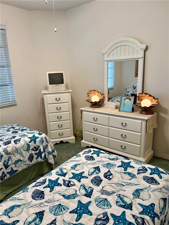 Bright bedroom featuring two beds with coordinating nautical-themed bedding, white wood-finish furniture including a dresser with multiple drawers and an arched mirror, pendant lighting, and carpeted flooring