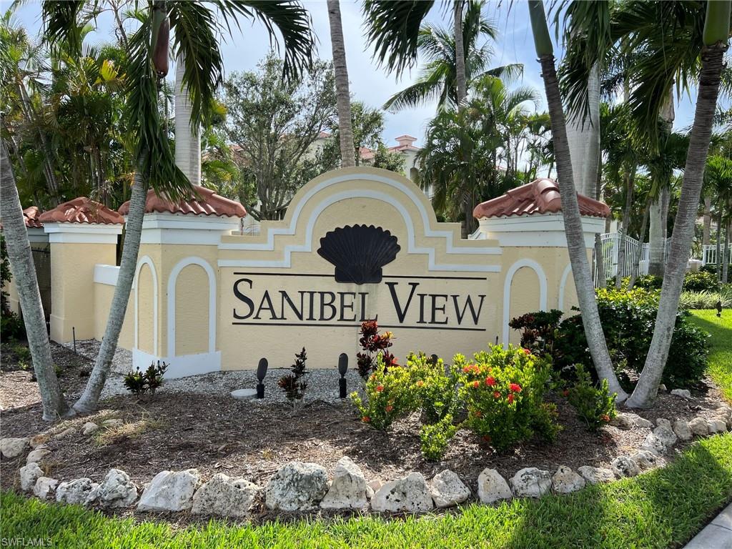 Sanibel View signage with decorative shell motif, flanked by mature palm trees, surrounded by vibrant landscaping, and a rock border