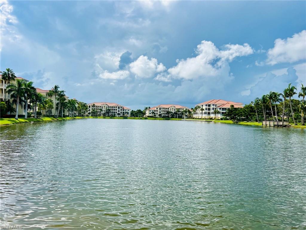 Expansive water feature with lush green landscaping, mature palm trees, and multi-story buildings featuring terracotta-style roofs