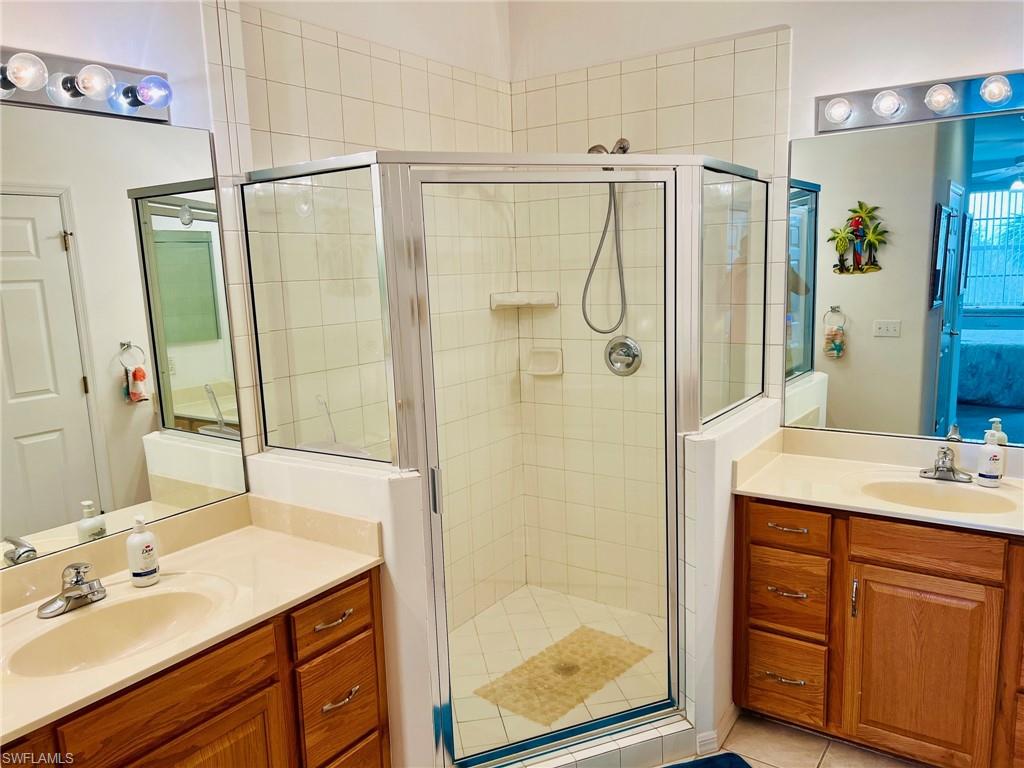 Master bathroom featuring dual wood-finish vanities with cream countertops, chrome faucet fixtures, and framed mirrors with integrated lighting