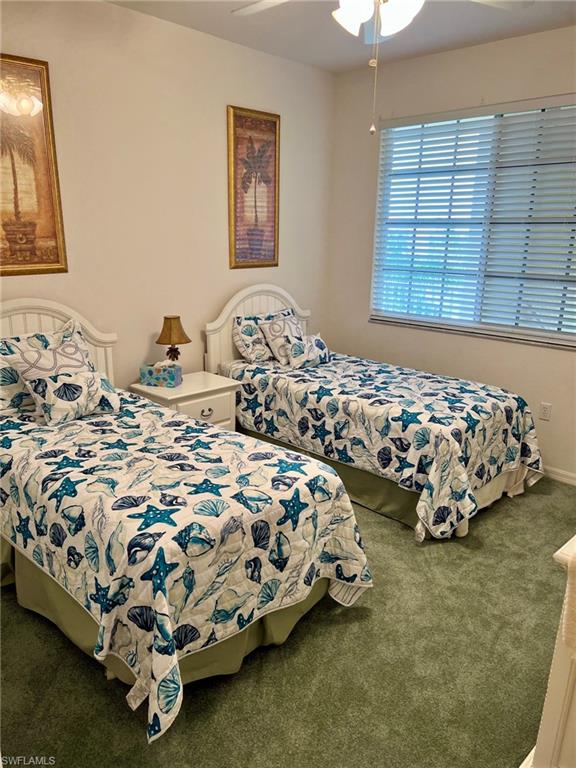 Dual beds with white headboards, green carpeting, white ceiling fan, and window with horizontal blinds