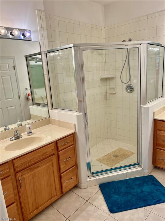 Master bathroom featuring a wood-finish vanity with dual sinks and ample countertop space, frameless glass shower enclosure with tile surround and integrated shelving, ceramic tile flooring, and recessed and wall-mounted lighting fixtures