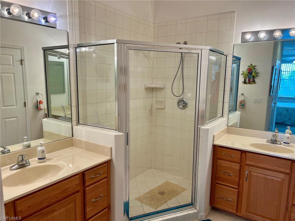 Dual wood-finish vanities with countertop sinks, a glass-enclosed corner shower with tiled walls, and reflective vanity mirrors with overhead lighting