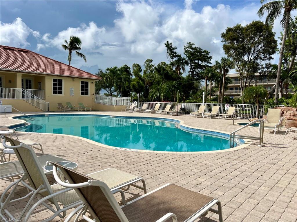 Resort-style pool with a paver deck, surrounding tropical landscaping, and a nearby building featuring a red tile roof
