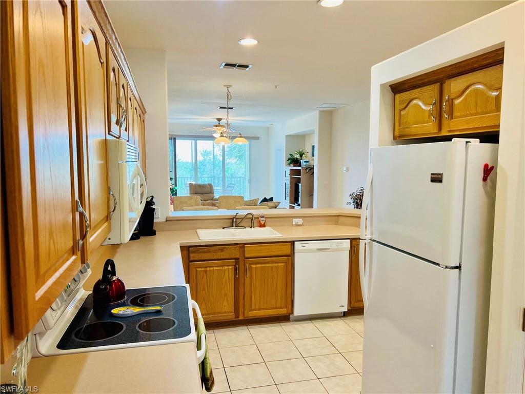 Kitchen featuring wood-finish cabinetry, white appliances, and a tile floor