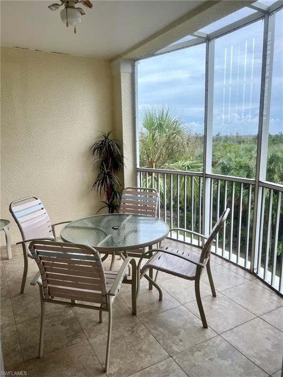 Screened balcony with tiled flooring, textured wall finish, and a ceiling fan