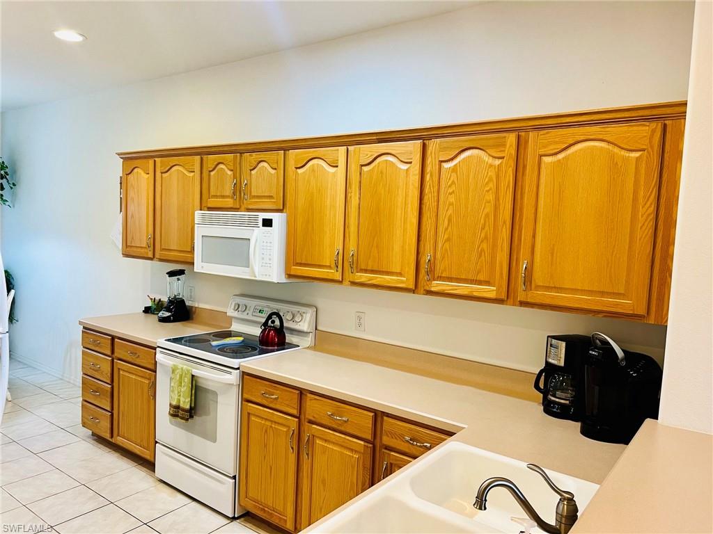 Kitchen featuring abundant wood cabinetry, an integrated white microwave, white electric range, and a double basin sink with a bronze-finish faucet