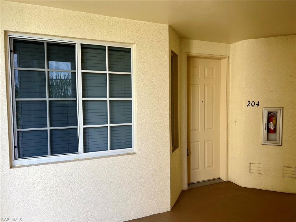 Window with grilles, textured exterior finish, recessed fire extinguisher cabinet, paneled entry door, and numerical unit identification