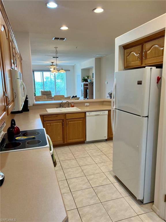 Kitchen featuring tile flooring, wood-finish cabinetry, built-in dishwasher, and a double basin sink