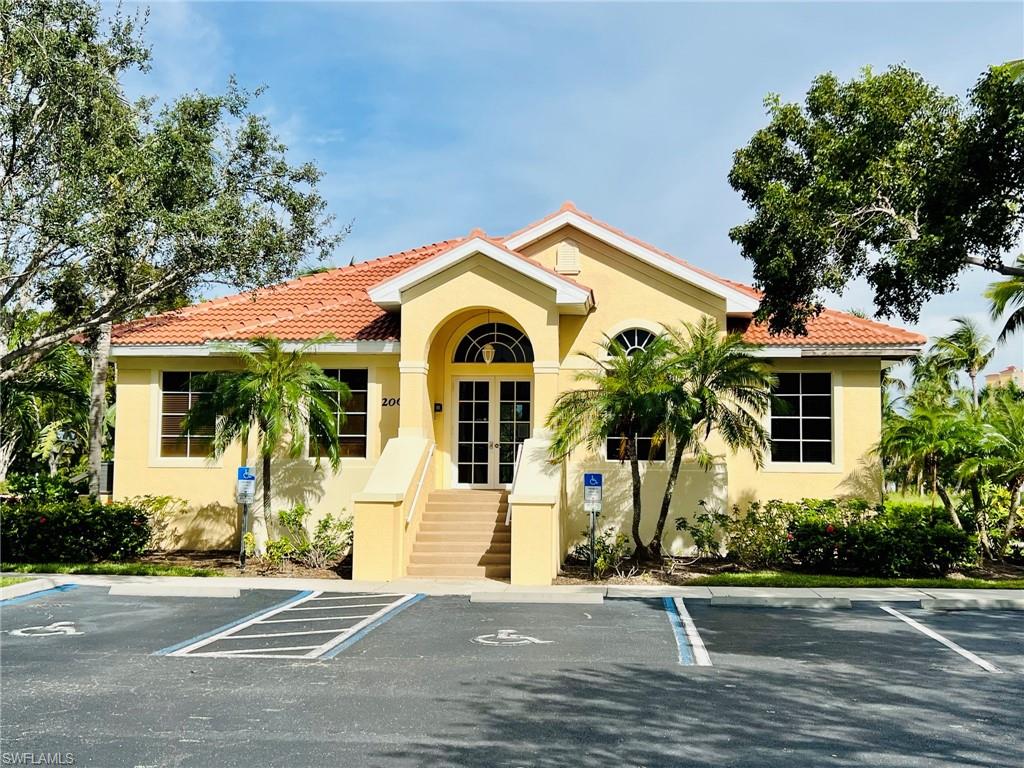 Stucco exterior featuring a red tile roof, arched entryway, double-door entrance, and surrounding landscaping