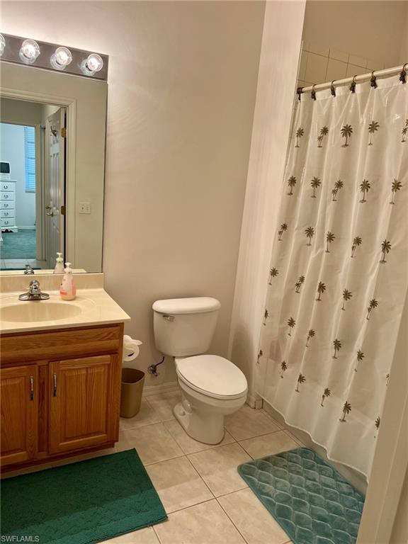 Bathroom featuring a vanity with wood-finish cabinetry, a single basin sink, a wall-mounted mirror, and a toilet