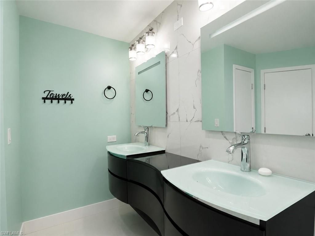 Dual vessel sinks with integrated glass countertops, sleek curved vanity cabinetry, wall-mounted mirrors, and marble-look wall tile