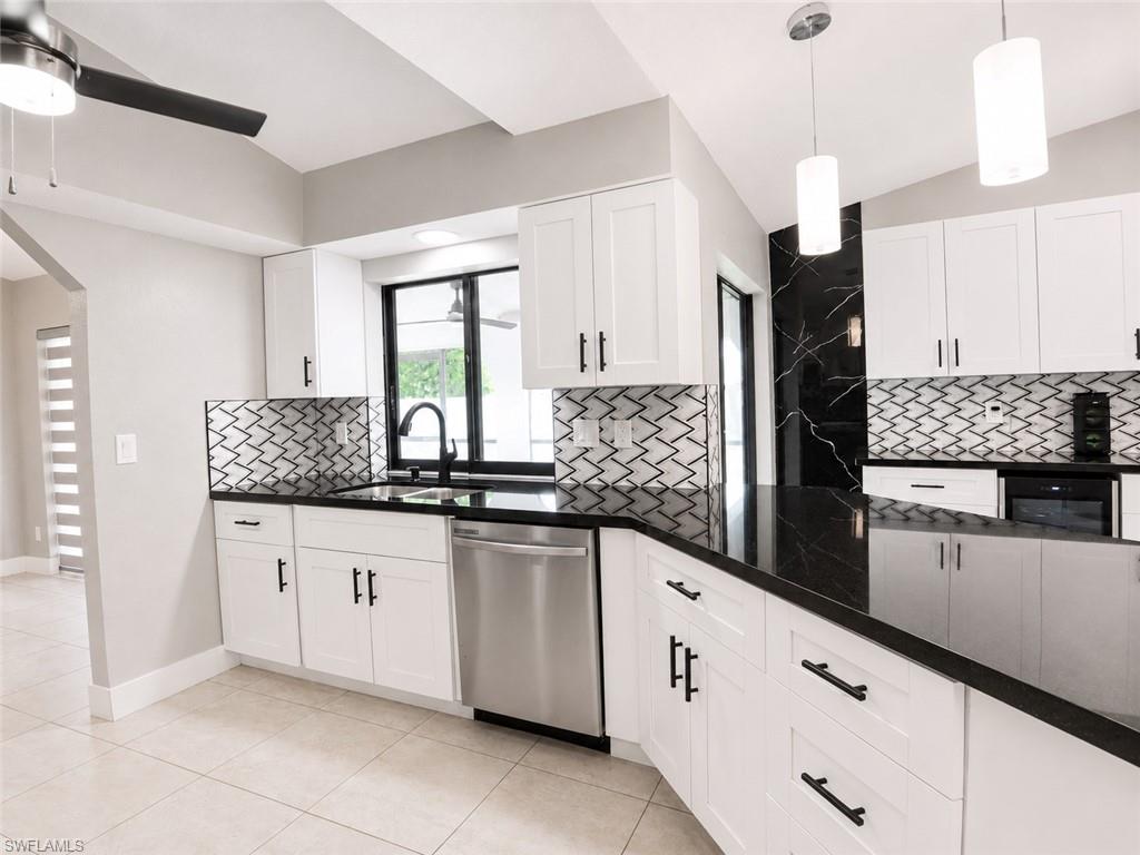 Kitchen featuring white shaker cabinetry, black countertops, stainless steel dishwasher, and geometric backsplash tiling