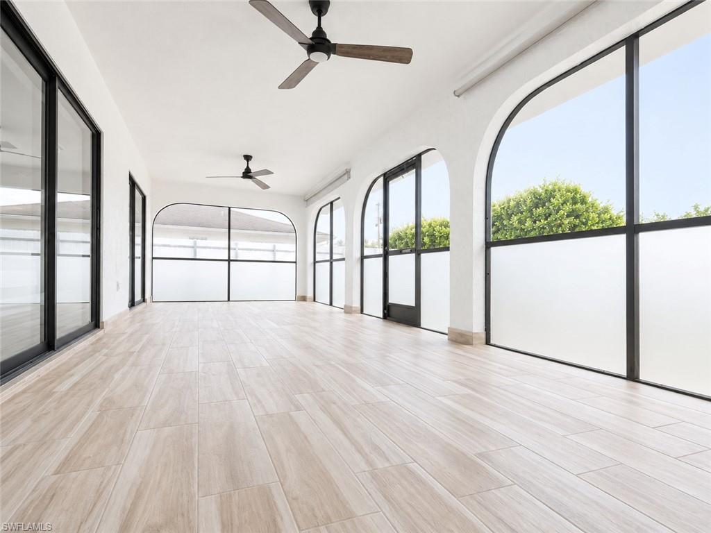 Arch-top windows with frosted lower panels, black frame sliding glass doors, light wood-finish flooring, and ceiling-mounted fans