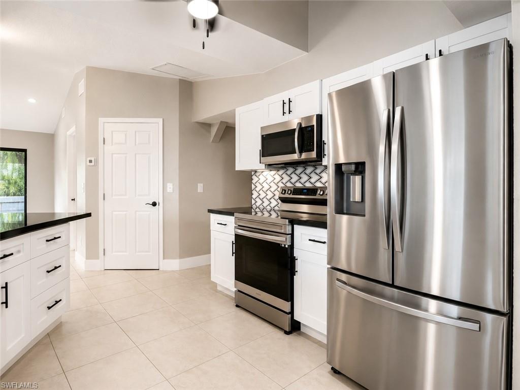 Kitchen featuring stainless steel appliances, white cabinetry, black countertops, a tile backsplash with a geometric pattern, and light-colored floor tiles