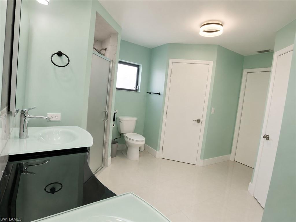 Contemporary bathroom featuring a vanity with an integrated sink, polished chrome faucet, tiled shower with a glass enclosure, white tile flooring, and a circular flush-mount ceiling light