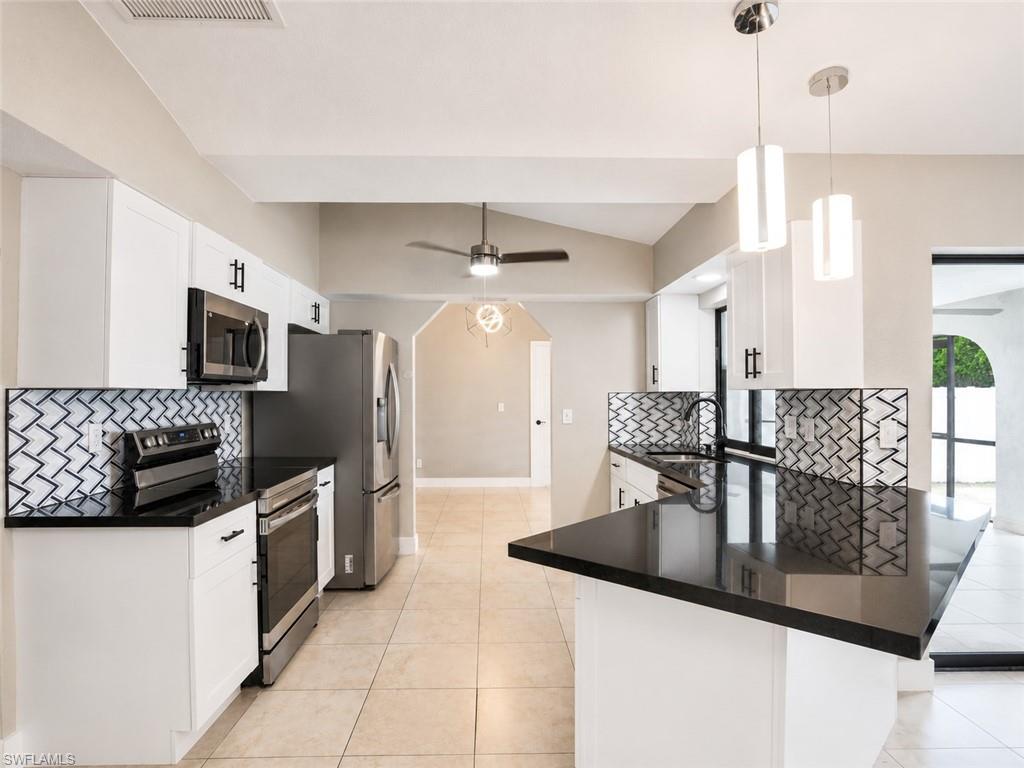 Kitchen featuring white cabinetry, stainless steel appliances, black countertops, a mosaic tile backsplash, and neutral tile flooring