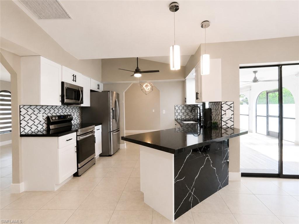 Modern kitchen featuring stainless steel appliances, black countertops, white cabinetry, and a geometric tile backsplash